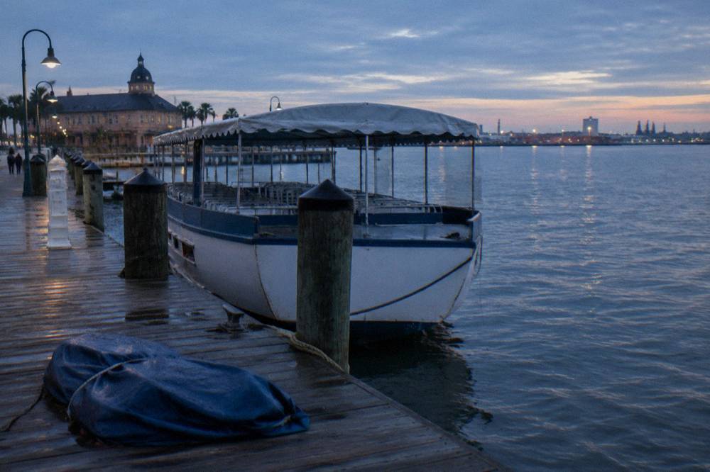 A covered tour boat tied at a wooden dock with harbor water and mooring lines in view