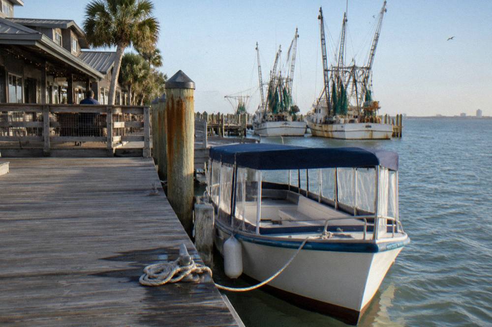 A small covered cruise boat tied at a wooden pier under a clear morning sky