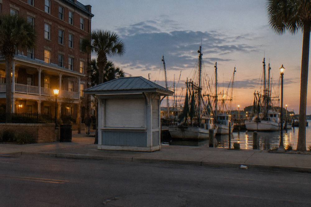 A ticket kiosk beside a hotel at a Galveston harbor pier with moored boats in the background