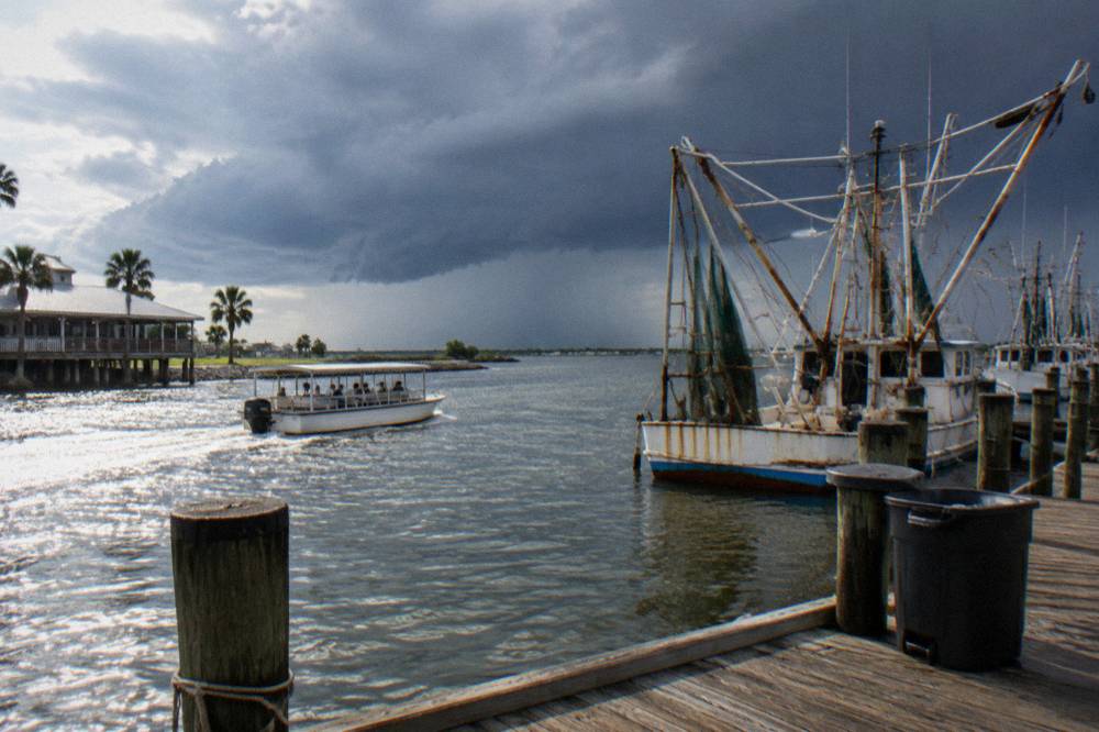 A small covered tour boat cruising past docked shrimp boats in a working Galveston harbor