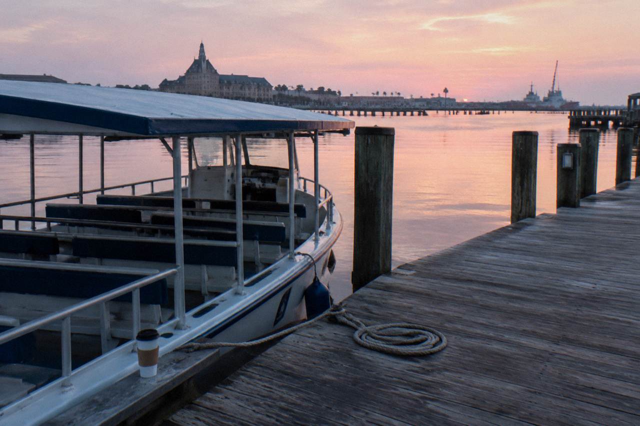 A covered sightseeing boat idle at a wooden pier on a calm Galveston harbor morning