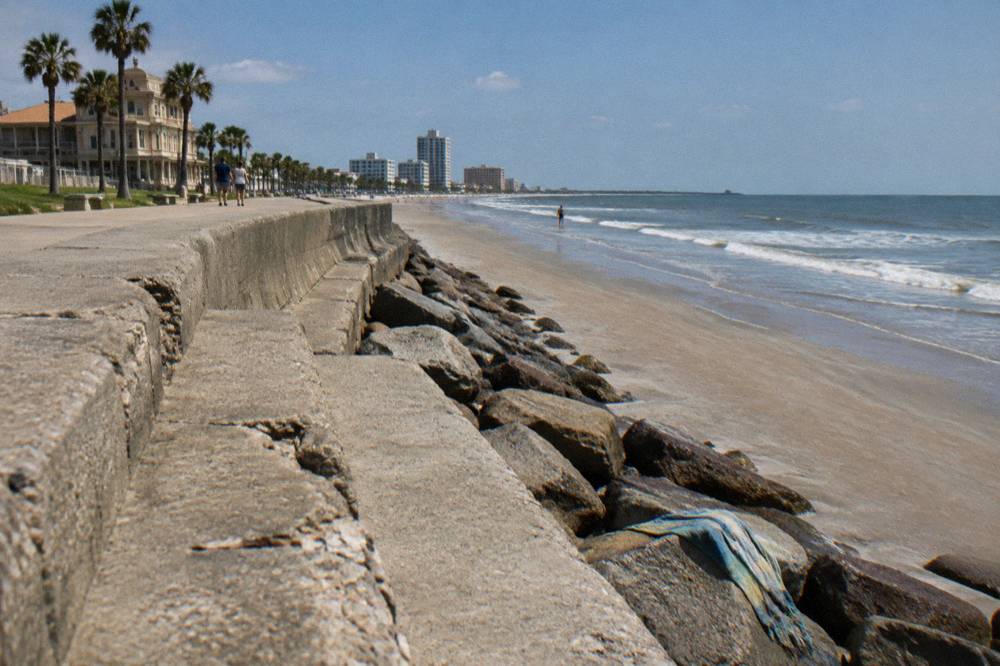 A wide concrete seawall curving along a sandy beach with gentle Gulf waves