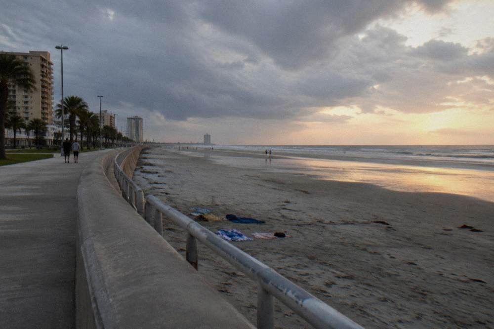 A long concrete seawall curving along a Gulf beach under a wide afternoon sky