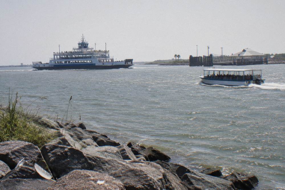 A tour boat and a ferry crossing open water in Galveston Harbor at midday