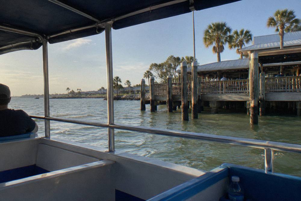Shaded seating area on a small covered tour boat with open side railings and bright sunlight on the water outside