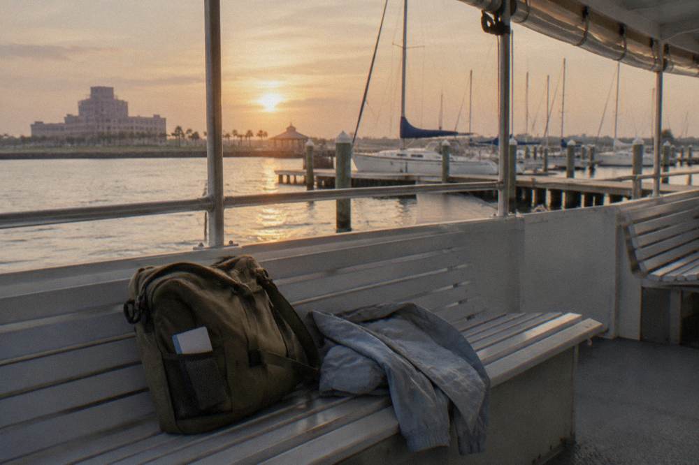 Small day bag and light jacket resting on a boat seat beside a railing with harbor water beyond