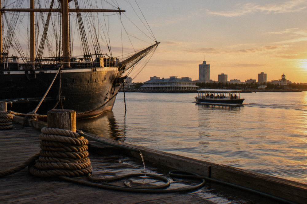 A small tour boat moving through a Galveston harbor channel at golden hour