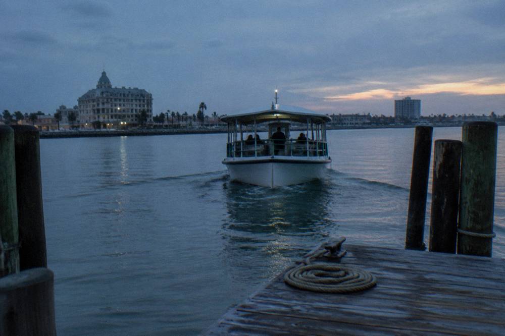 A small passenger boat leaving a Galveston pier under early morning light