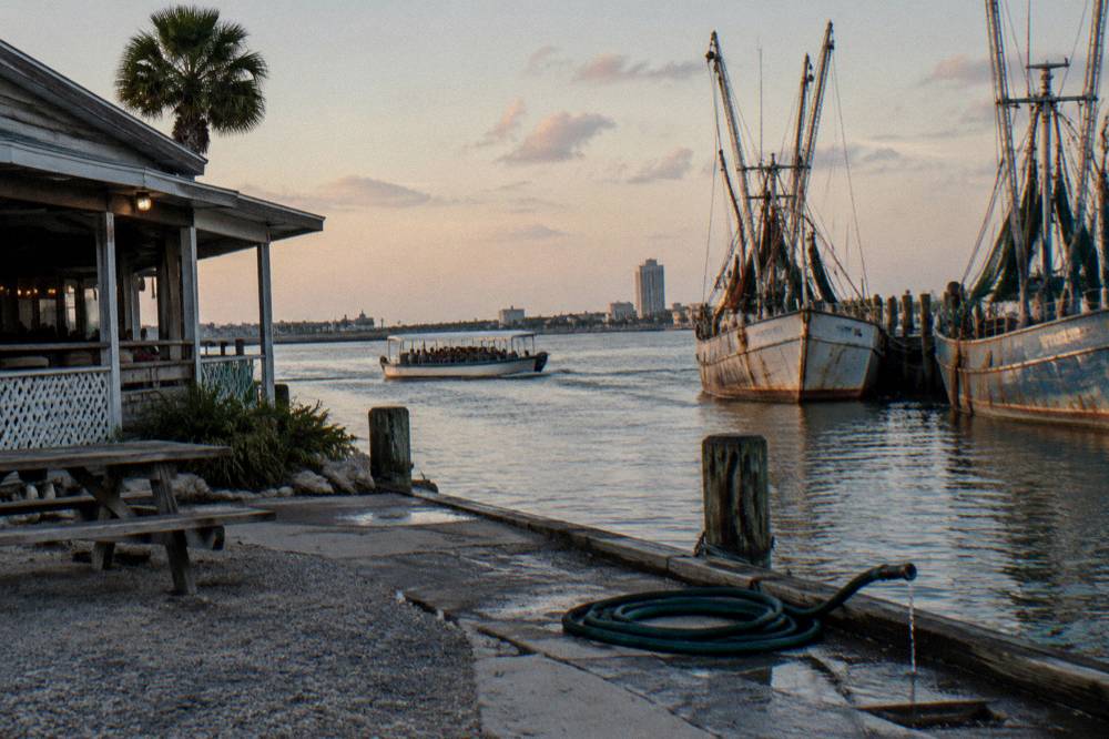 A harbor channel in Galveston with a tour boat passing moored fishing vessels