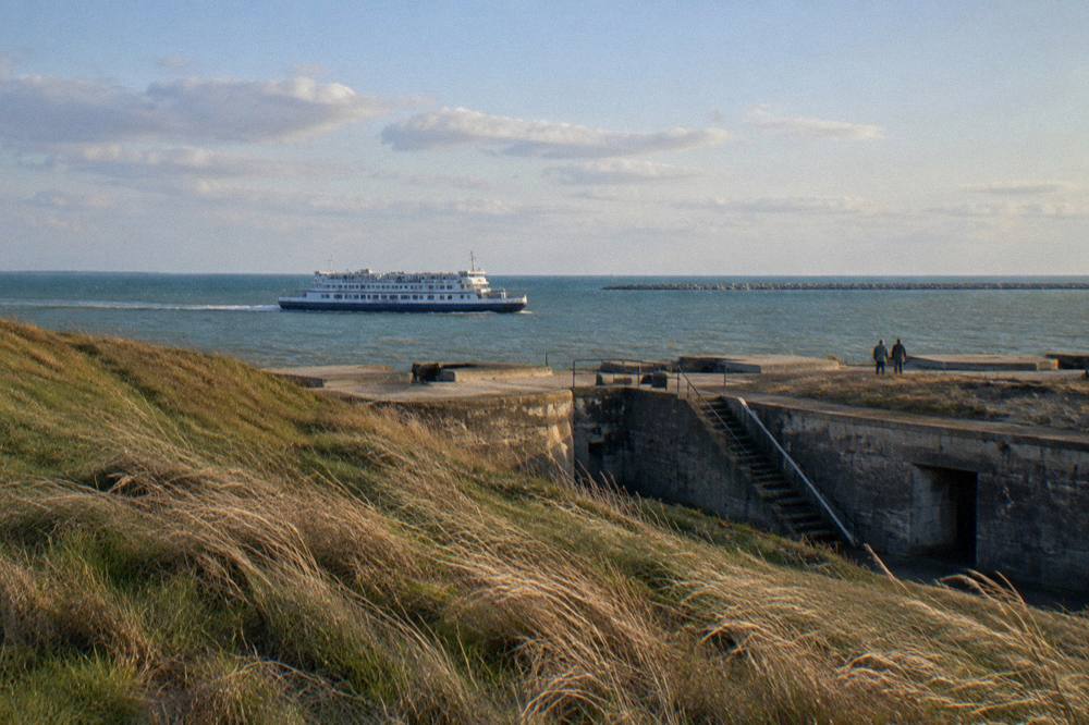 A ferry boat crossing open channel water with a long breakwater in the distance