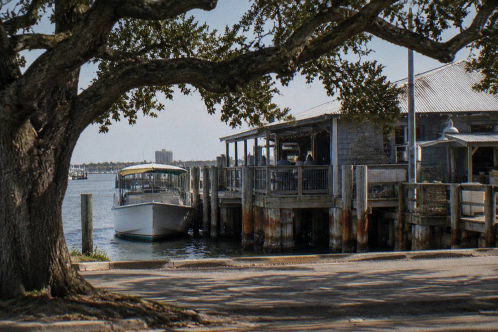 A small covered tour boat tied at a wooden pier beside a hotel in a working harbor