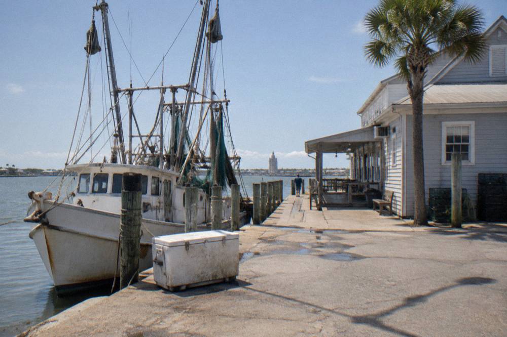 A fishing boat docked beside a seafood market building along a harbor road