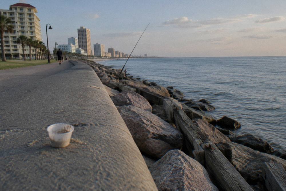A wooden jetty extending into calm Gulf water beside a wide seawall promenade