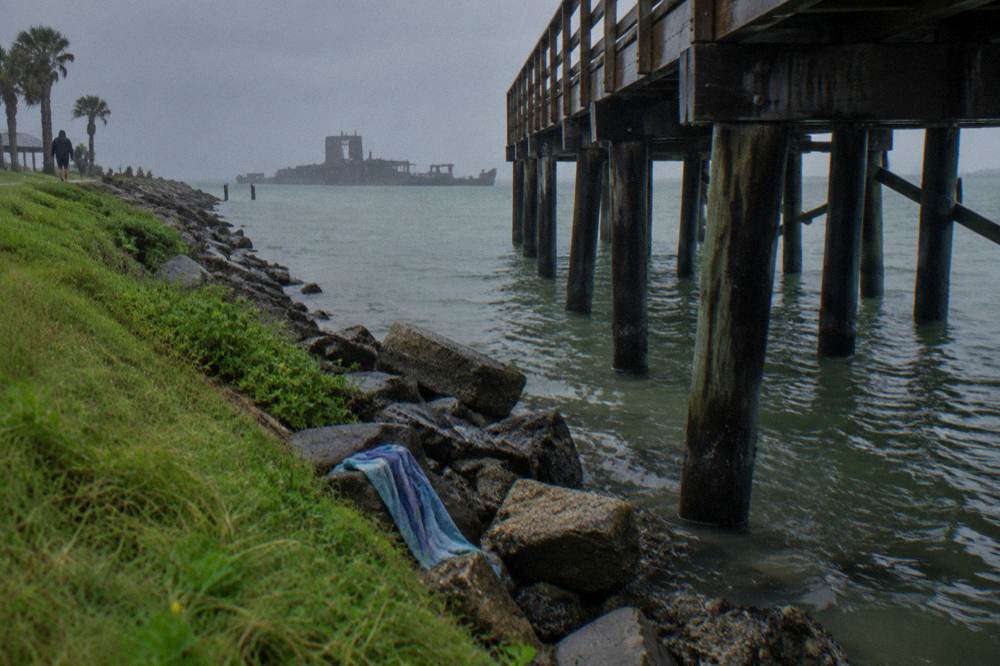 A fishing pier over channel water with distant ships and an open horizon