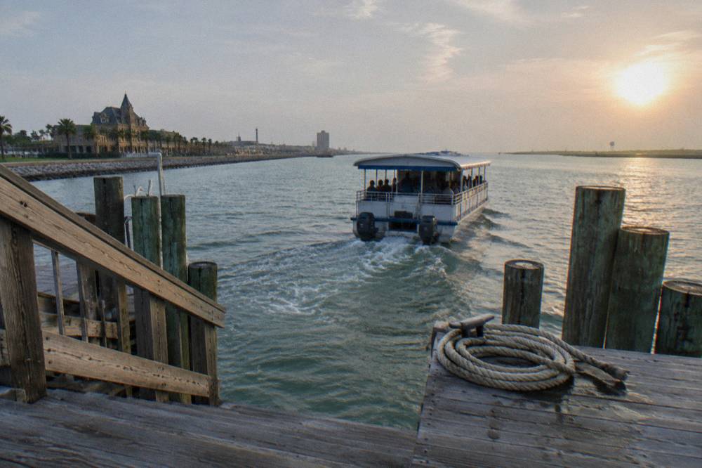 A covered passenger boat departing a Galveston pier with the harbor channel ahead