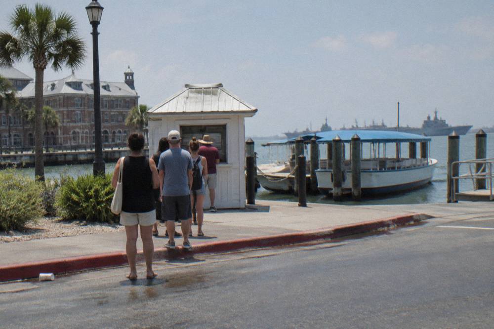 A line of visitors waiting at a harbor kiosk beside a moored tour boat