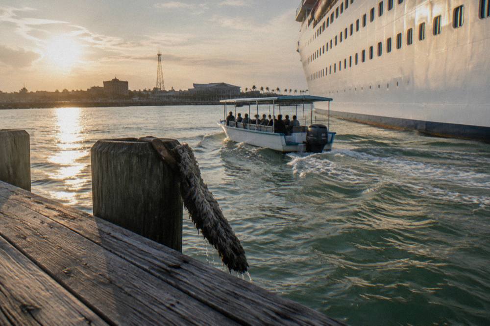 Dolphin tour boat cruising past docked ships in a Galveston harbor channel