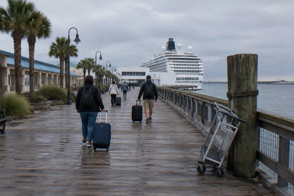 Passengers walking along a harbor boardwalk toward a cruise terminal entrance