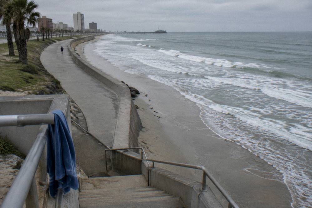 A wide concrete seawall curving along a Gulf beach with gentle waves and an open sky