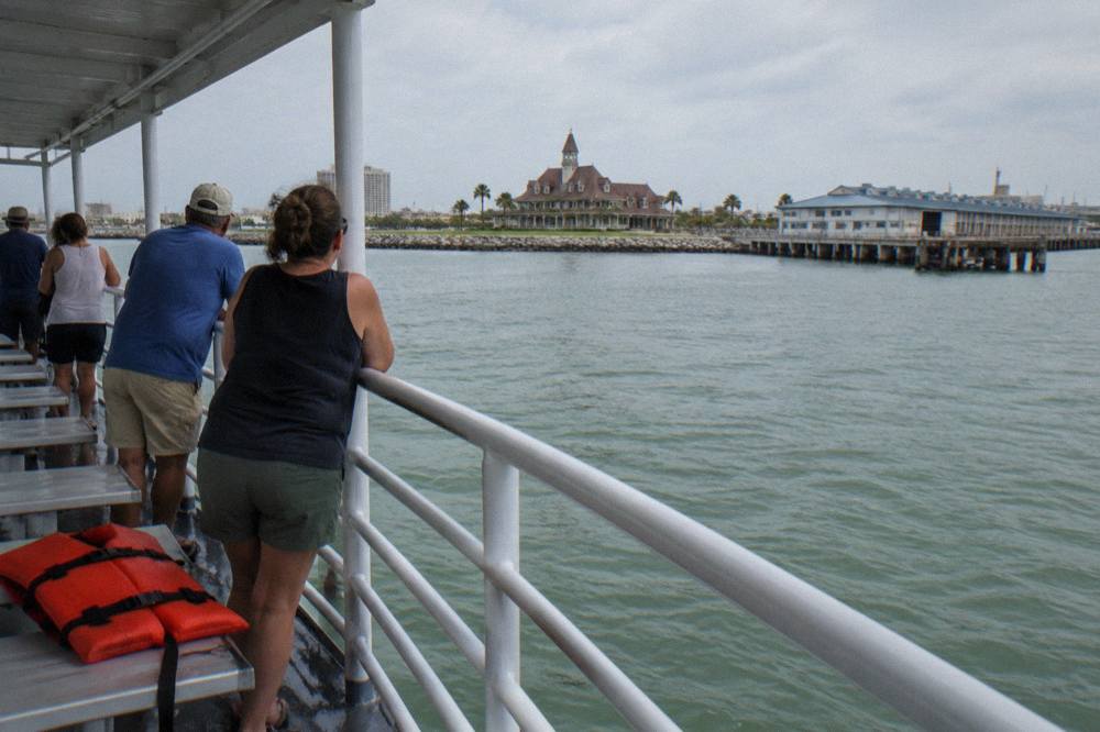 Passengers leaning on the rail of a covered tour boat watching calm harbor water