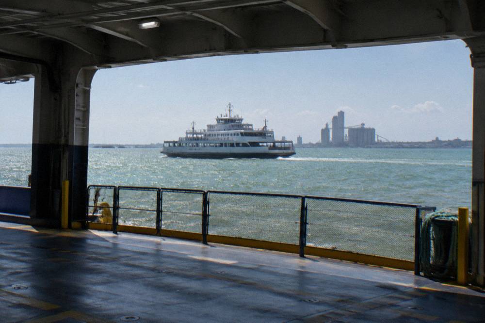 A state ferry crossing a wide ship channel with open water and distant docks