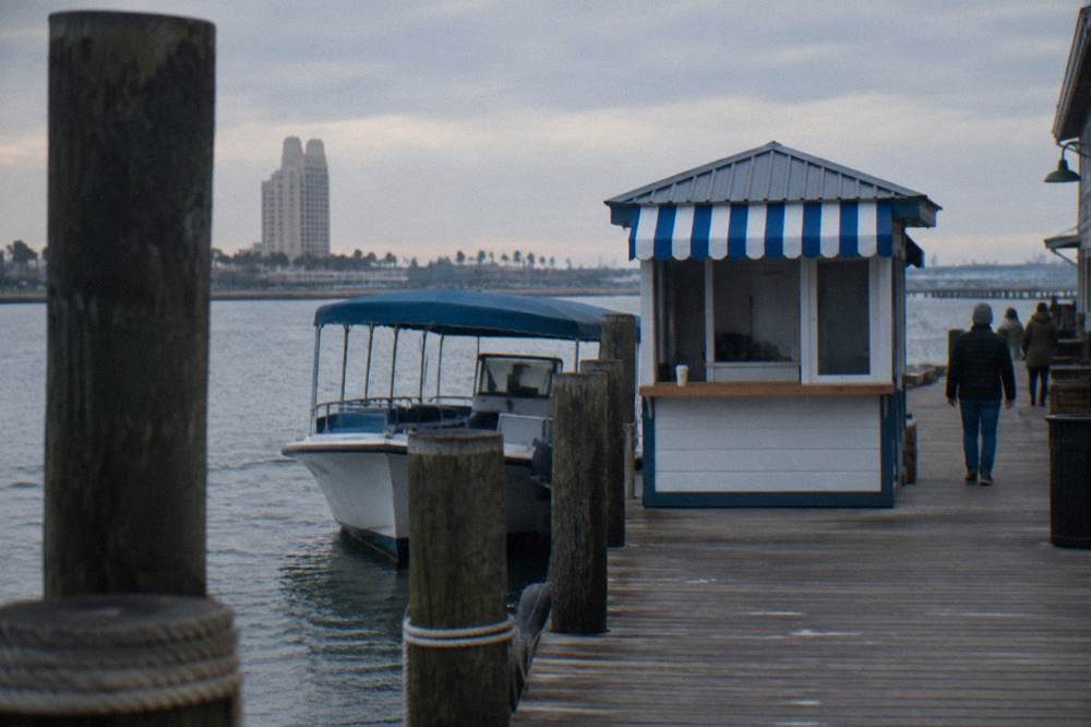 A ticket kiosk beside a harbor dock with a tour boat tied up behind it