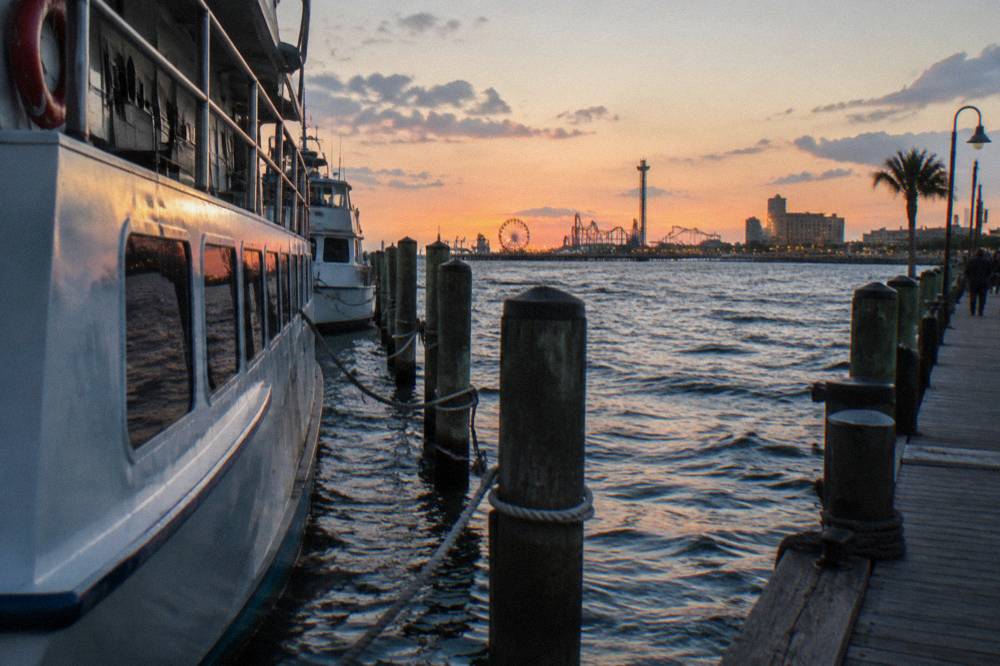 Dolphin tour boats moored at a harbor pier with the Seawall skyline in evening light