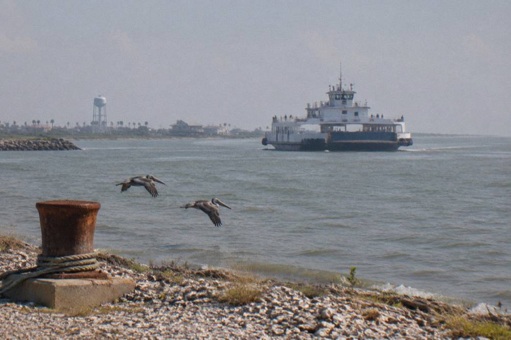A ferry vessel underway on open bay water with passengers standing along the rail