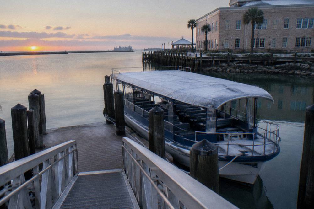 A covered tour boat at a harbor dock with calm water and a clear sky