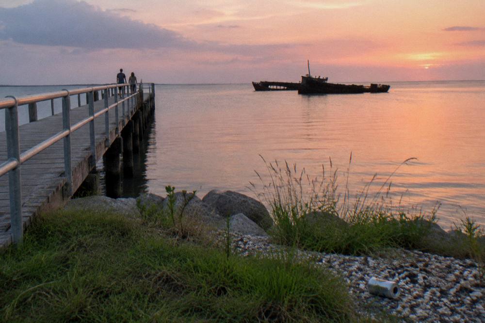 A quiet shoreline park with a pier extending into calm bay water at dusk