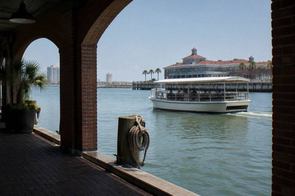 A covered tour boat on calm harbor water with railings along the open sides