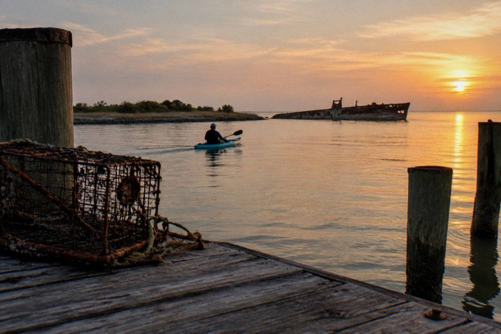 A kayak gliding across a quiet bay at golden hour with harbor industry in the distance